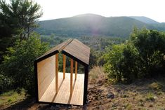 a small wooden structure sitting on top of a hill next to trees and bushes with mountains in the background