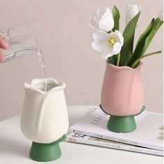 a person pouring water into a vase with flowers in it on top of a table