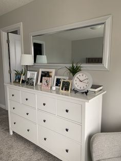 a white dresser topped with lots of pictures and a clock on it's side