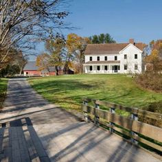 a large white house sitting on top of a lush green field next to a wooden bridge