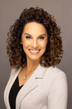 a smiling woman with curly hair and a gray blazer is posing for the camera