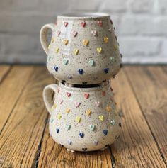 two ceramic mugs are stacked on top of each other, with colorful sprinkles all over them