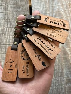 a hand holding several wooden keychains that say dad and have been engraved on them