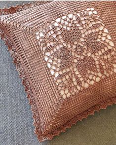 two brown pillows with crocheted designs on them sitting on a gray couch cushion