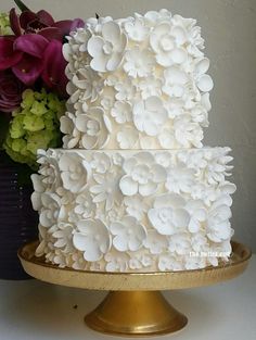 a three tiered wedding cake with white flowers on the side and gold plated stand