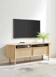 a flat screen tv sitting on top of a wooden entertainment center next to a plant