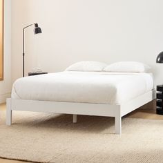 a white bed sitting on top of a wooden floor next to a black table lamp