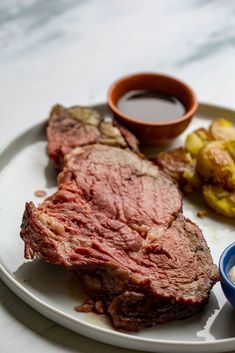 a white plate topped with steak, potatoes and dipping sauce