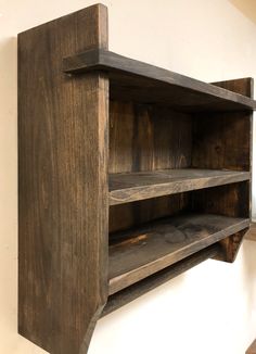 a wooden shelf with two open shelves on the top and bottom, against a white wall