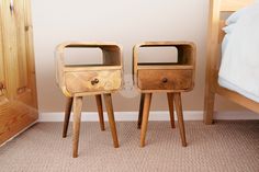 two wooden nightstands sitting next to each other on the floor in front of a bed