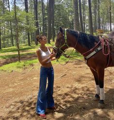 a woman standing next to a brown horse in the middle of a forest with trees