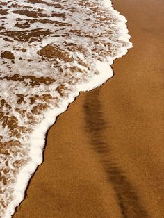 an ocean wave rolls in on the beach sand and shore line with white foamy water