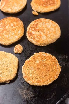 several pancakes are being cooked on a black pan with some other food items in the background