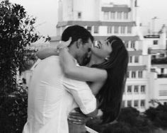 a man and woman embracing each other in front of some buildings with the city behind them