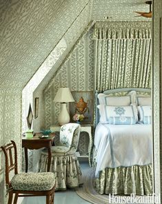 a bed sitting under a window next to a chair and table in a room with white walls