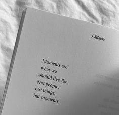 an open book sitting on top of a bed next to a white sheet with the words, moments are what we should live for not people, not things, but moments