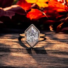 a diamond ring sitting on top of a wooden table in front of autumn leaves and foliage