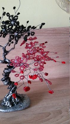 a wire tree with red berries on it sitting on a wooden table next to a vase