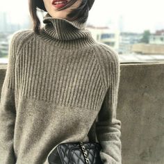 a woman wearing a turtle neck sweater holding a black handbag in front of her face