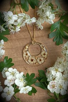 a necklace with flowers and leaves around it on a wooden table next to white flowers