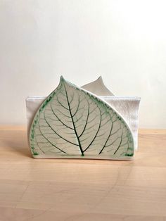 a green leaf shaped dish sitting on top of a wooden table next to a white wall