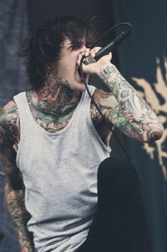 a man with tattoos on his arms and chest holding a microphone to his mouth while singing