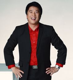 a man in a black suit and red shirt standing with his hands on his hips