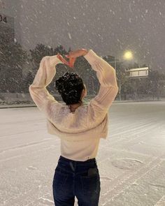 a woman standing in the snow making a heart with her hands