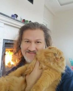 a man holding a cat in front of a fire place