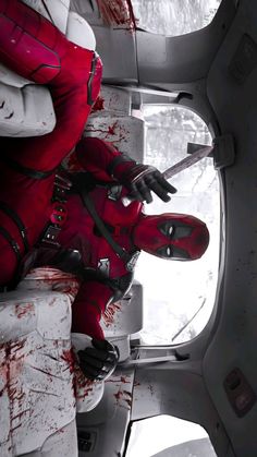 a man dressed in red and white with blood all over his body sitting on a plane