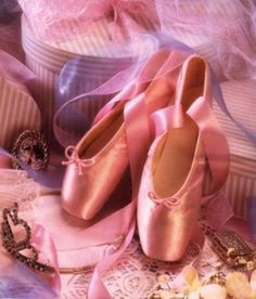 two pairs of pink ballet shoes sitting on top of a pile of ribbon and ribbons