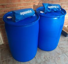 two large blue barrels sitting in front of a brick wall with the words aquamamma on them