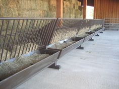 several metal benches with hay in them on the side of a barn floor next to a building