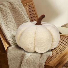 a large white pumpkin sitting on top of a wooden chair next to a knitted blanket