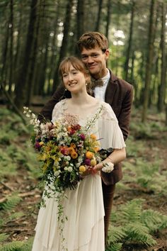 a man and woman are standing in the woods holding bouquets with flowers on them