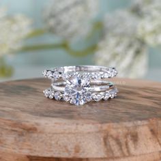 two wedding rings on top of a wooden board with flowers in the background and white flowers behind them