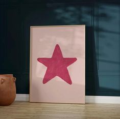 a pink star is on the floor next to a brown vase and a framed photograph