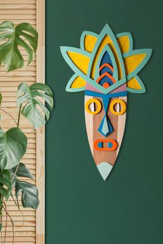 a wooden mask hanging on the side of a green wall next to a potted plant