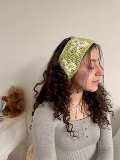 a woman with curly hair wearing a green crochet headband sitting on a bed