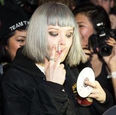 a woman with grey hair holding a white object in front of her face and surrounded by people