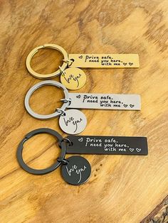 three different key chains on top of a wooden table with some writing on the tags