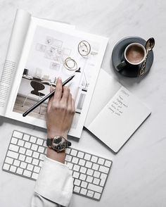 a person is writing on a book next to a keyboard and coffee cup with a pen