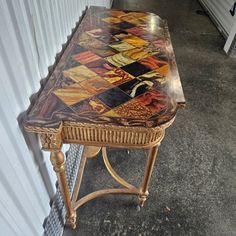 a wooden table with an artistic design on it's top and legs, sitting in front of a white wall