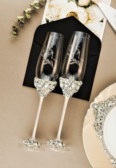 two wine glasses with silver glitters on them sitting next to a plate and napkin