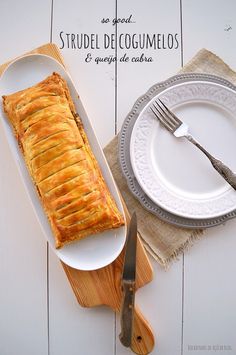 a white plate topped with a pastry next to a knife and fork on top of a wooden cutting board