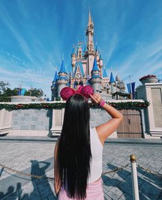 a woman standing in front of a castle with minnie ears on it's head