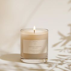 a candle with a label on it sitting in front of a white wall and shadow