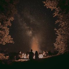 people sitting around a campfire with the night sky in the background