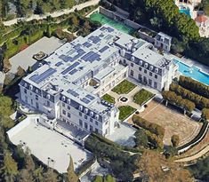 an aerial view of a large white mansion surrounded by trees and greenery in front of a swimming pool