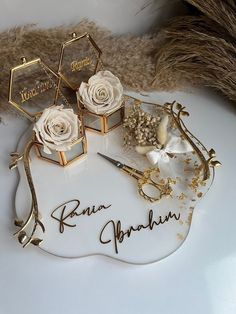 two white roses sitting on top of a table next to some gold and silver items